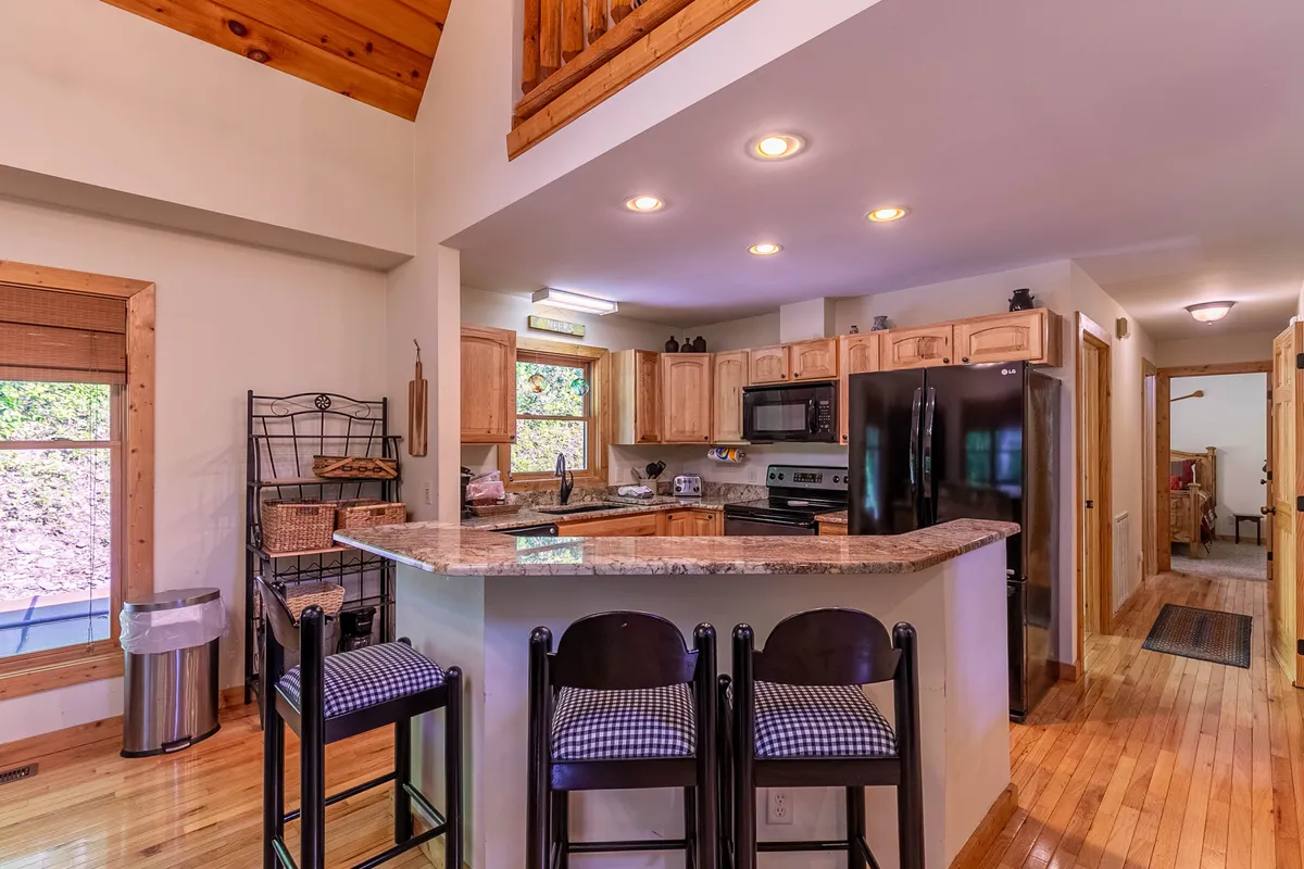 A stylish gourmet kitchen featuring granite countertops, wooden cabinetry, stainless steel appliances, and bar stools. The open layout allows for easy interaction between the kitchen and adjacent living spaces, perfect for entertaining and casual dining.