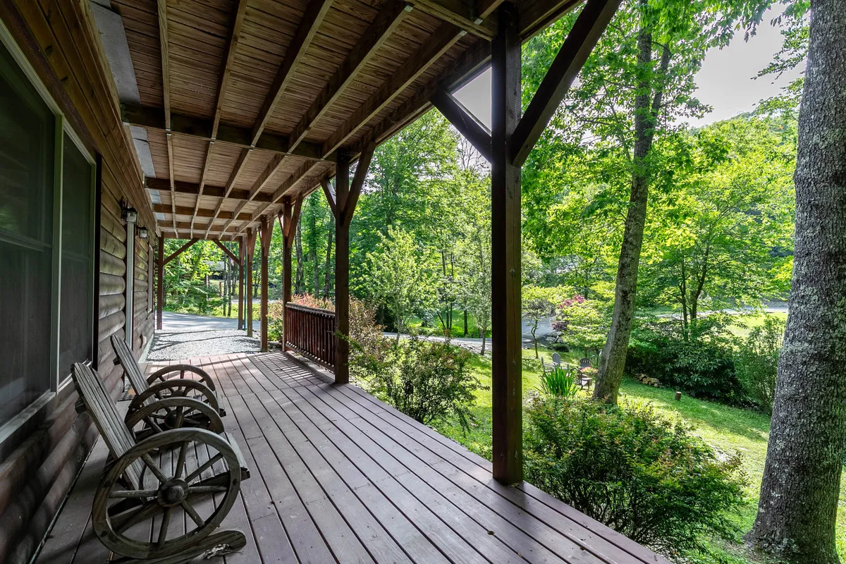 This exterior image features classic wooden rocking chairs on a covered porch, with sturdy wooden beams and lush greenery surrounding the space. The chairs face outward, inviting guests to relax and take in the natural mountain scenery.