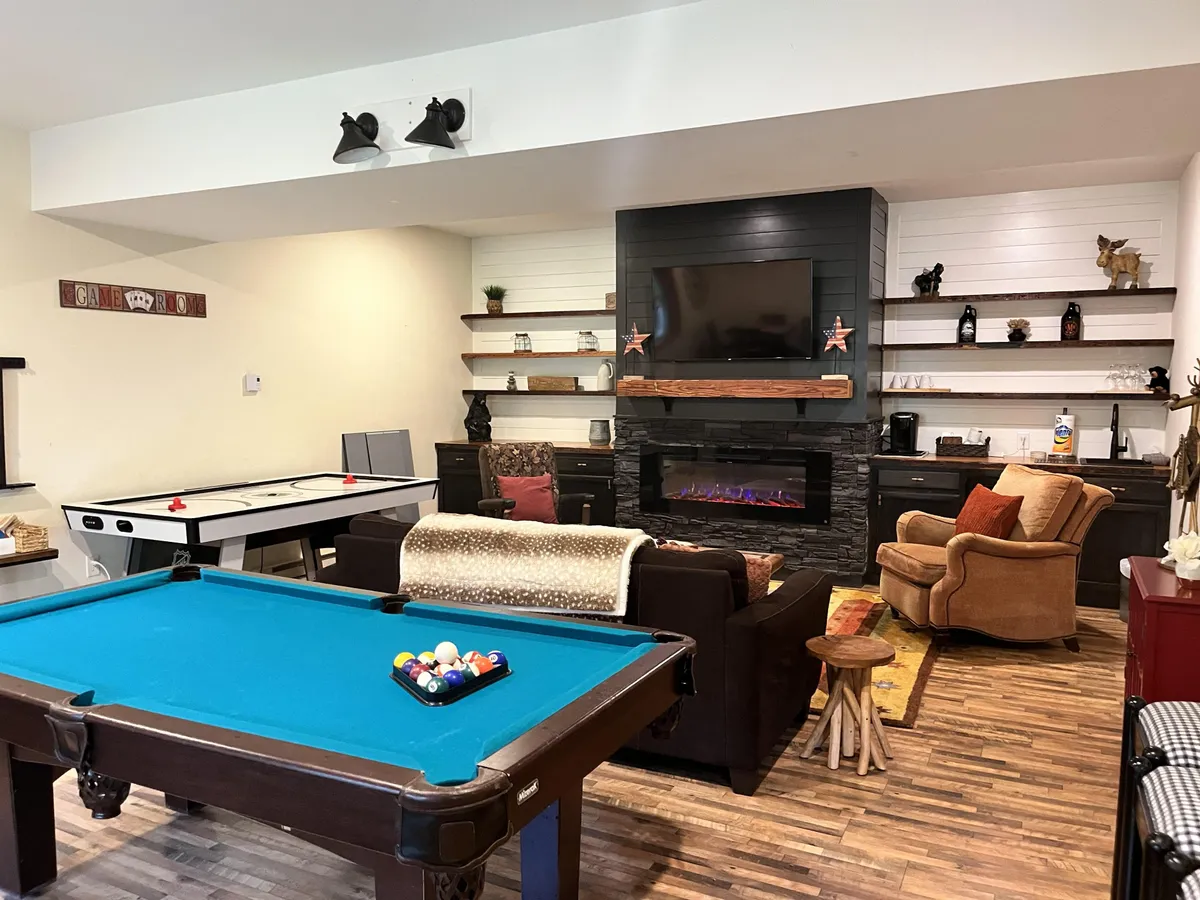 A warm and inviting game room with a pool table, air hockey table, fireplace, stylish shelving, and comfortable seating. The room's casual ambiance is perfect for game nights or relaxing after the excitement.