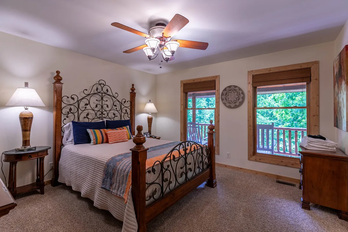 A cozy bedroom with an ornate bed frame adorned with colorful pillows, complemented by soft lighting from bedside lamps and sunlight streaming through windows. The space is tranquil, inviting relaxation and restful sleep.