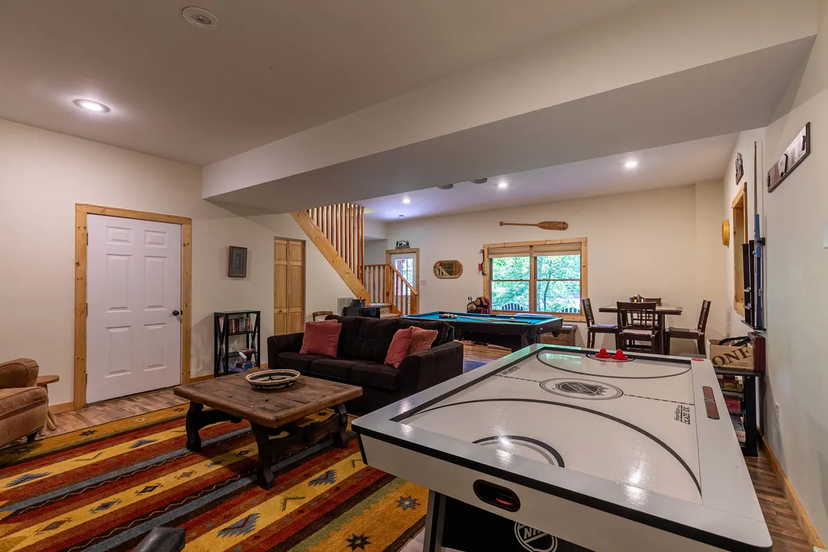 A vibrant game room with an air hockey table, pool table, and comfortable sofa seating. Large windows invite natural light and offer glimpses of the outdoors, emphasizing fun and togetherness inside, rain or shine.