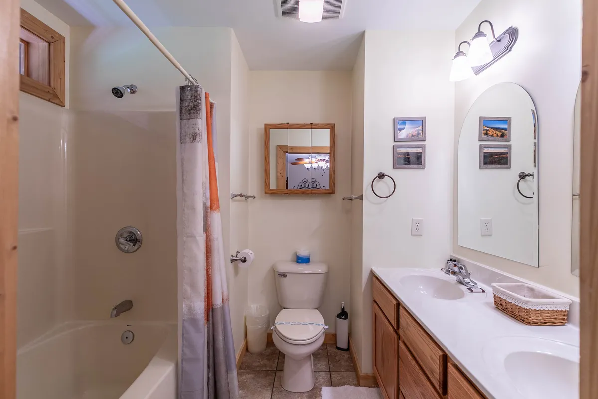 A modern bathroom with double sinks, a framed mirror, a shower area, and a toilet. The layout is organized and inviting, ideal for refreshing after game nights or movie marathons.