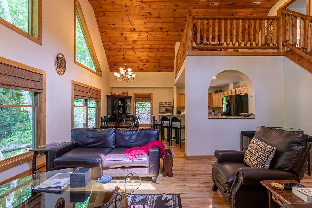 A cozy combined living and dining area with a comfortable sofa, a family-sized dining table, expansive windows, and a wooden ceiling. The natural light and outdoor views create an inviting atmosphere perfect for gatherings and relaxation.