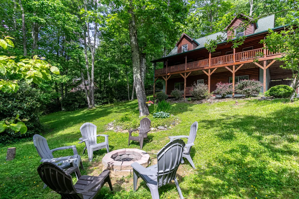A charming log cabin nestled among tall trees, featuring a welcoming fire pit surrounded by cozy outdoor seating. The inviting wooden house stands at the heart of a spacious yard, perfect for gathering with friends or family, with nature's beauty all around.