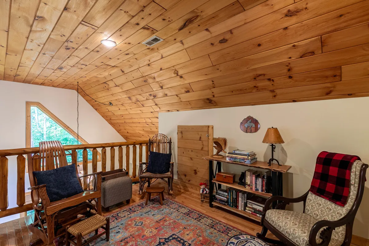 A tranquil reading loft with a wooden ceiling, built-in bookshelf, and a comfortable seating area. The cozy setting is ideal for quiet reading sessions or solitary escapes above the main living areas.