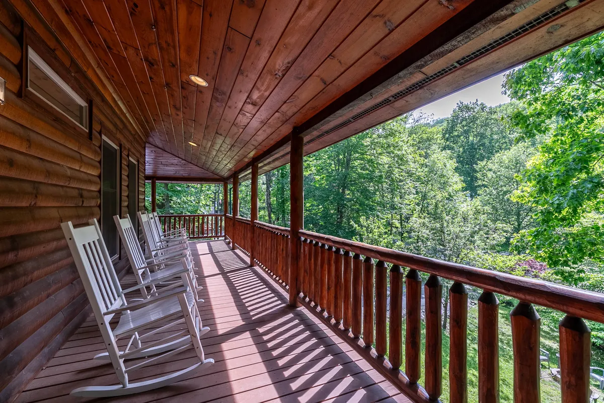 This image highlights a tranquil porch scene with wooden rocking chairs and a rustic railing overlooking lush greenery. Although not snow-covered, it suggests the cabin’s inviting outdoor spaces for relaxing after a day of adventure.