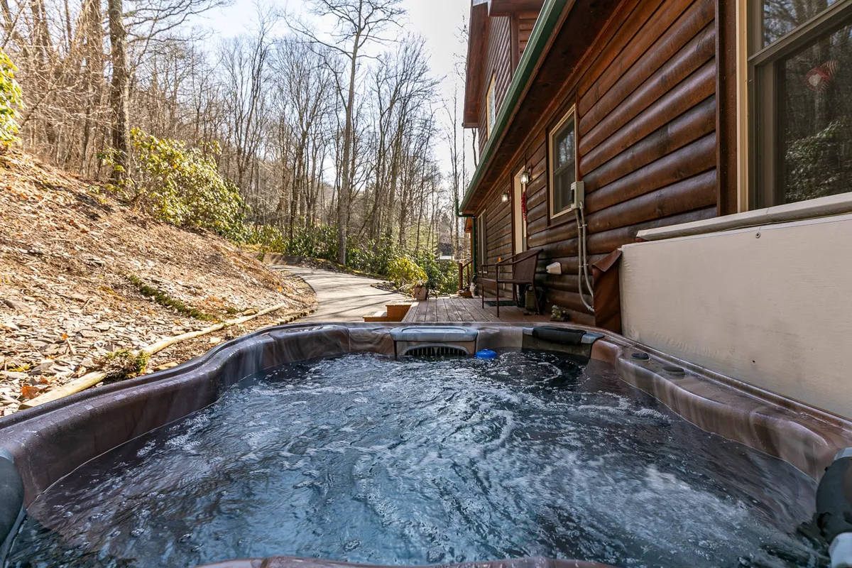 This image captures a peaceful scene of the cabin’s exterior, surrounded by trees, with a luxurious hot tub in the foreground. The hot tub is positioned for stargazing or morning relaxation, and the cabin’s rustic architecture is visible, emphasizing its connection to nature.