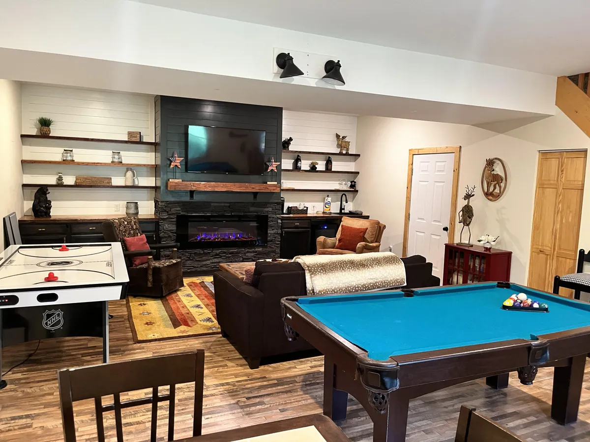 A lively game room featuring a pool table, air hockey table, fireplace, and a television. The space is furnished with a comfortable couch, creating a versatile environment for family tournaments, friendly competitions, and movie marathons.