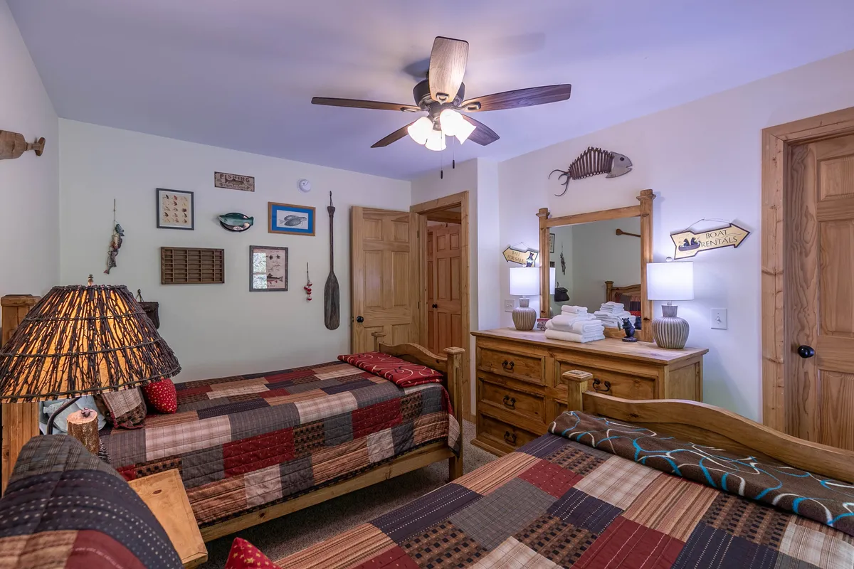 A cozy bedroom with two beds adorned with colorful patchwork quilts, a decorative lamp, a wooden dresser, and a wall mirror. The inviting setup suggests a comfortable space for friends or family to share while fostering late-night talks and relaxation.