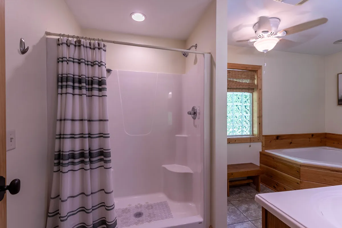 A serene bathroom featuring a spacious bathtub and a window letting in natural light, alongside a modern shower area and ceiling fan. The tranquil environment sets the scene for relaxation and rejuvenation after group adventures or celebrations.