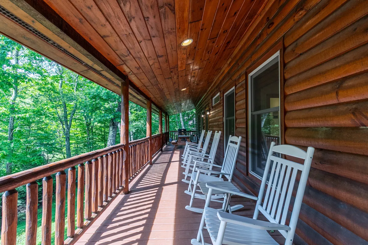 Another inviting porch scene with wooden rocking chairs and a rustic railing, surrounded by vibrant greenery. The view hints at a peaceful, private setting ideal for relaxation and conversation after a day outdoors.