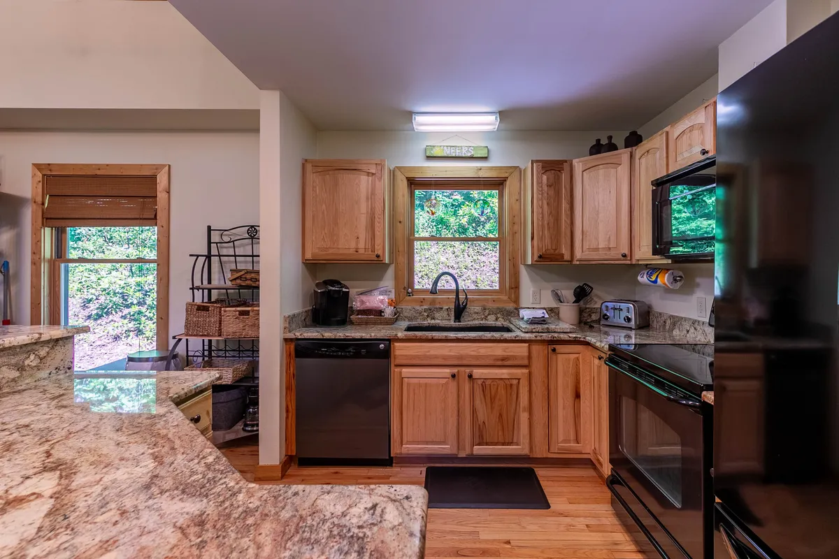 A spacious kitchen with granite countertops, warm wooden cabinetry, and a window that offers a glimpse of the outdoors. The space is arranged for group gatherings, with room for cooking, entertaining, and enjoying meals together.